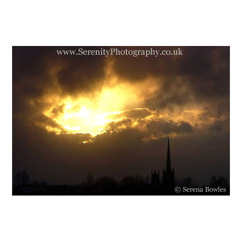 The sun breaks through the clouds above a church spire. Northern England.